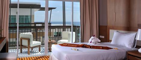 Quarto de hotel com uma cama grande, uma mesa, uma cadeira e varanda com vista para o mar.