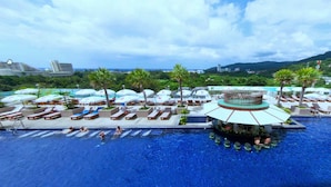 Área de piscina em resort com vários espreguiçadeiras e guarda-sóis, cercada por vegetação exuberante e paisagem montanhosa.