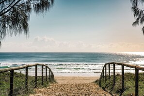 Un sentier qui longe la plage et mène à l’océan, avec une clôture en bois de chaque côté.