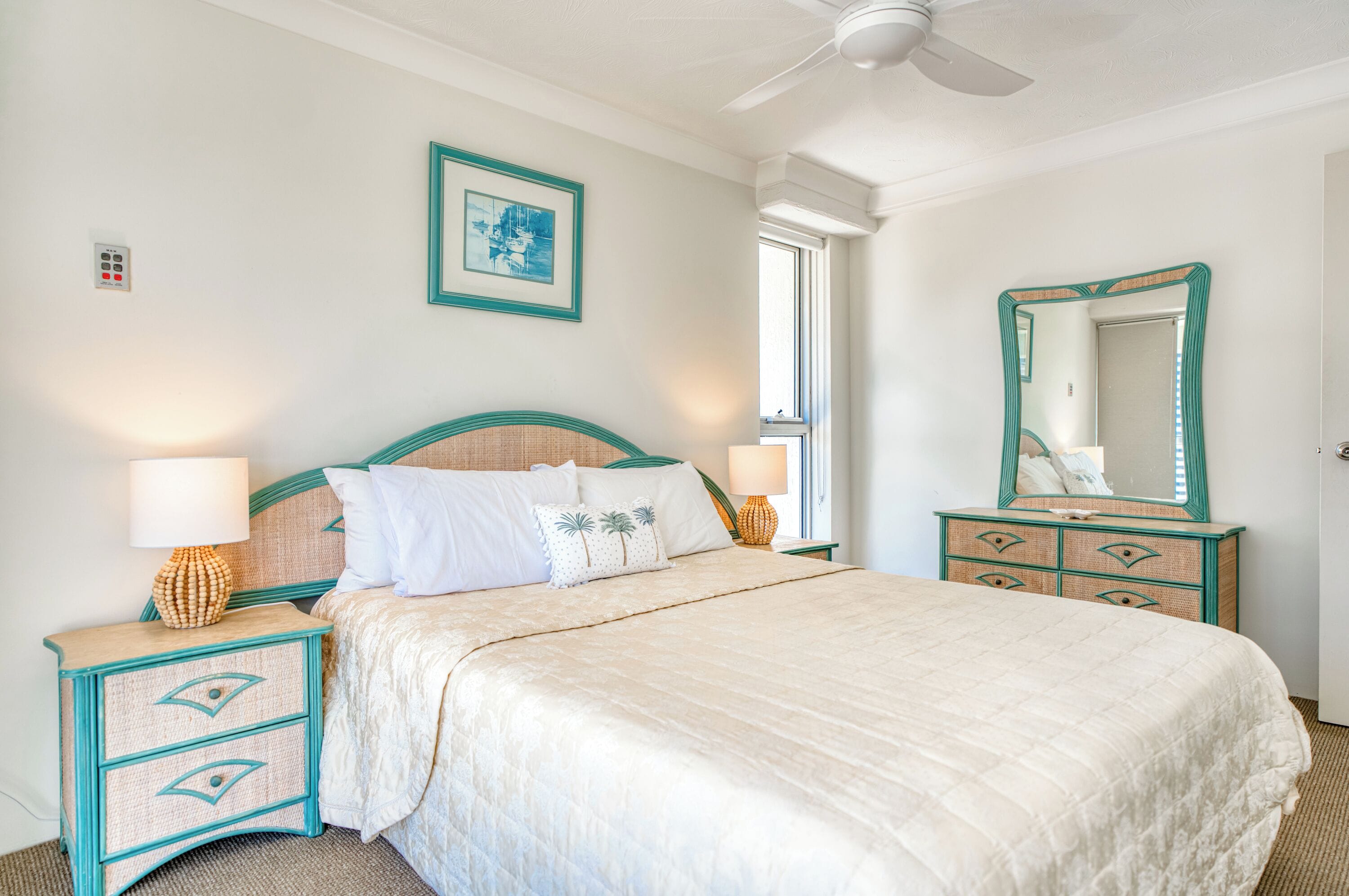 A neatly arranged bedroom with a bed, bedside lamps, a dresser, and a mirror.