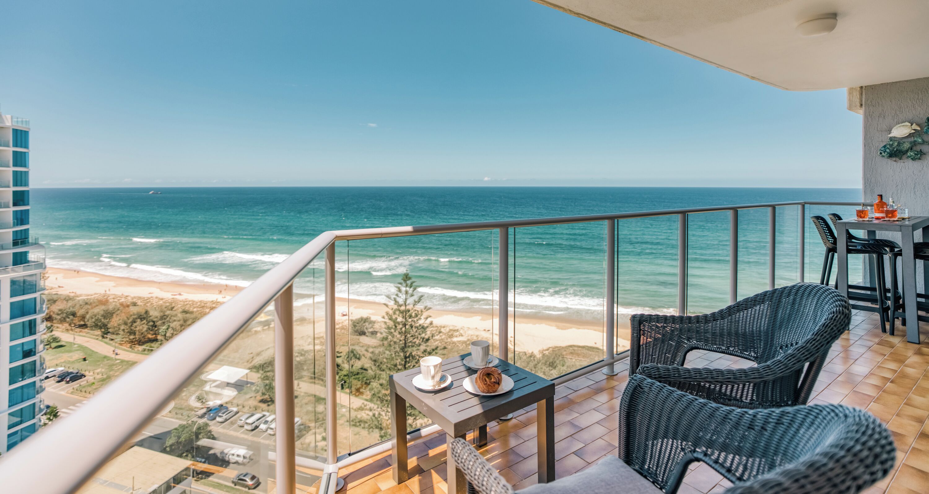 A balcony with a view of the ocean, wicker furniture, and a table with a drink and a plate.