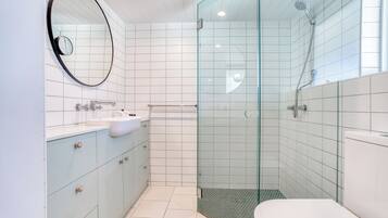 Un baño moderno con ducha de vidrio, un espejo redondo y armarios azul claro.