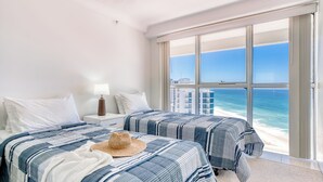 Habitación de hotel con dos camas, un ventanal con vista al océano y una playa.