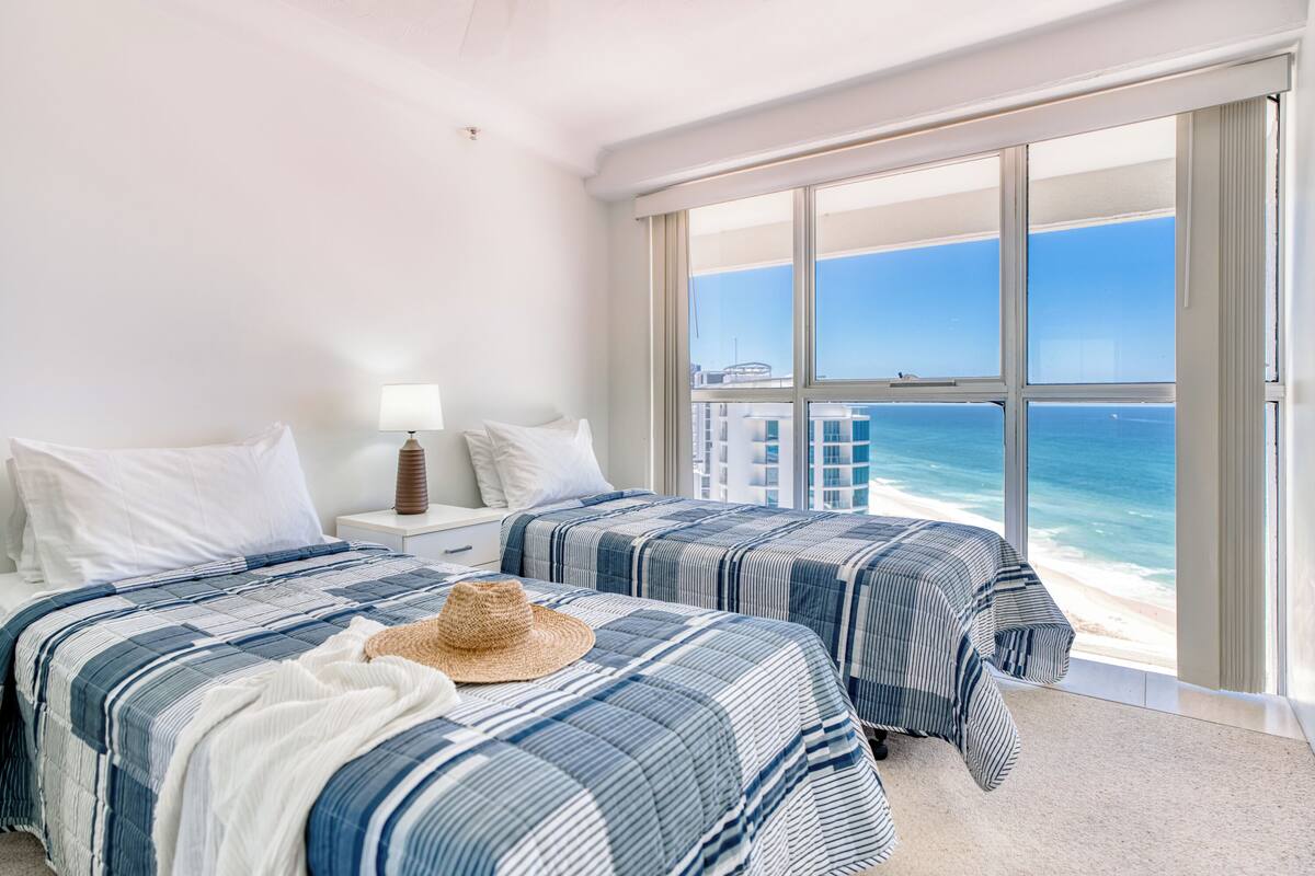 A hotel room with two beds, a large window with a view of the ocean, and a beach.