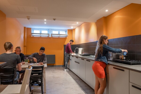 A modern kitchen with a central island, a dining area with four chairs, and a window providing natural light. - a&o Hamburg City - Hostel (Hamburg)