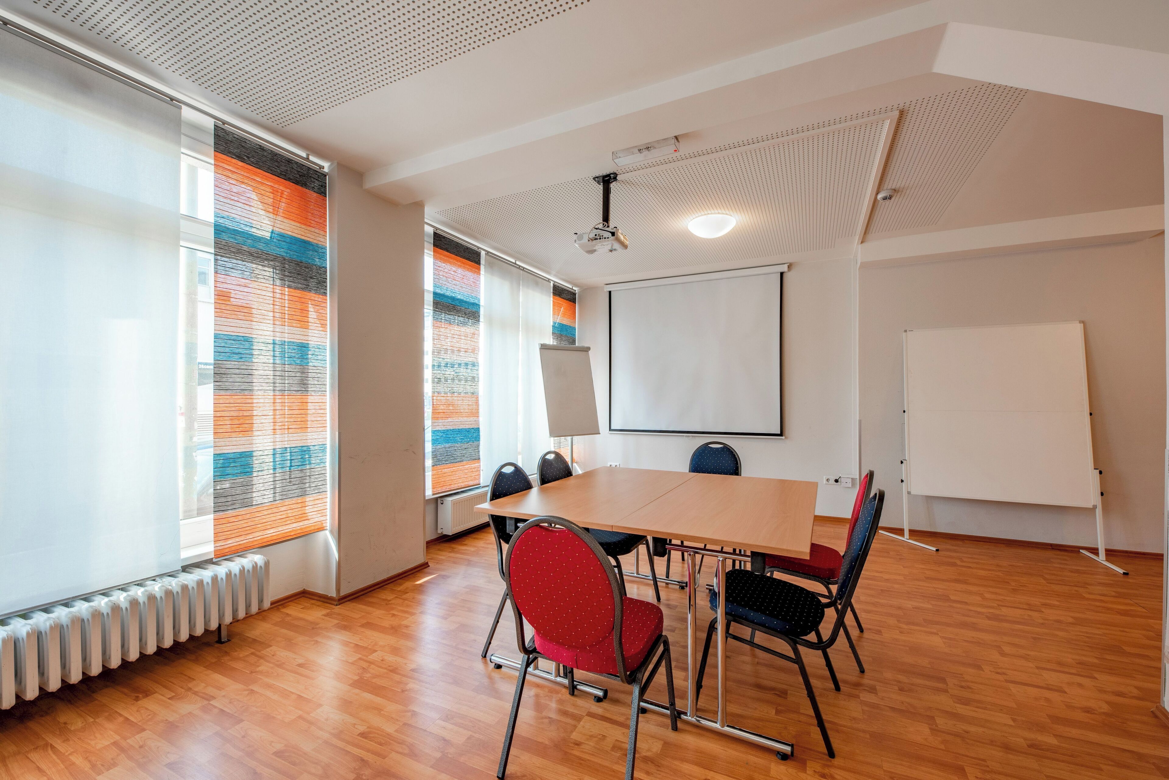Un salón de conferencias con una mesa grande, cuatro sillas, una pizarra y un proyector.