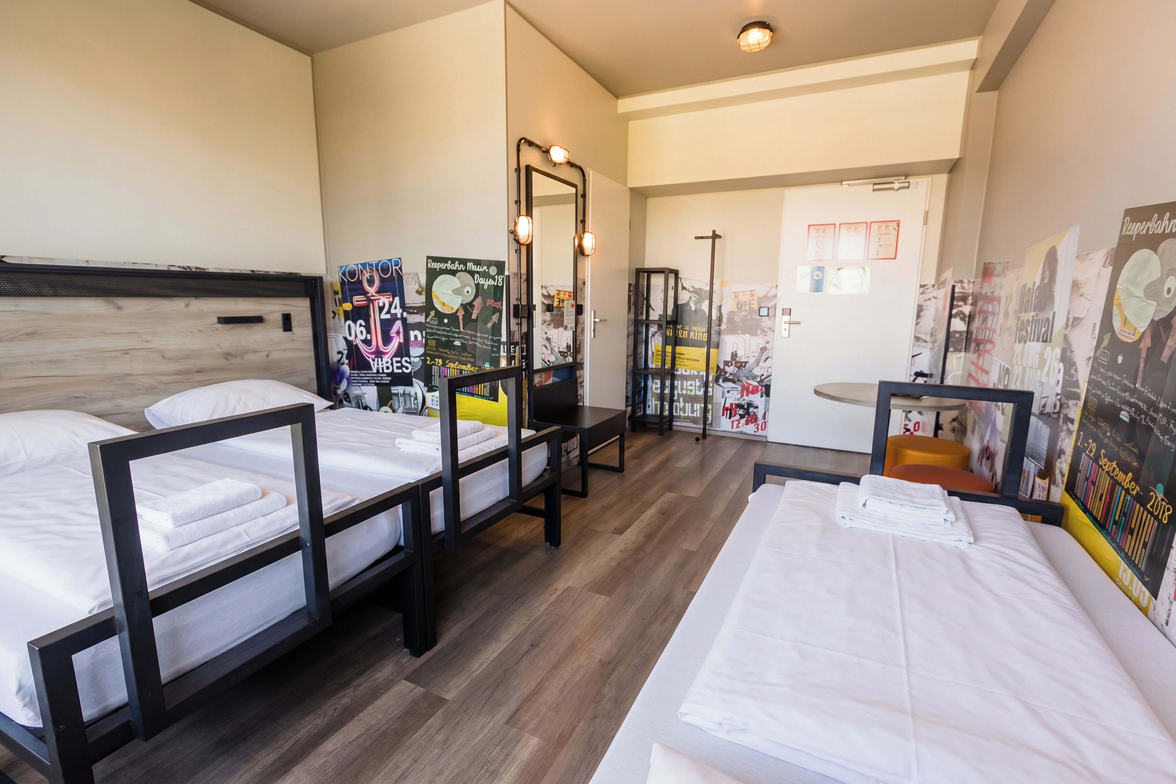 A hotel room with three beds, a small table, and posters on the walls.