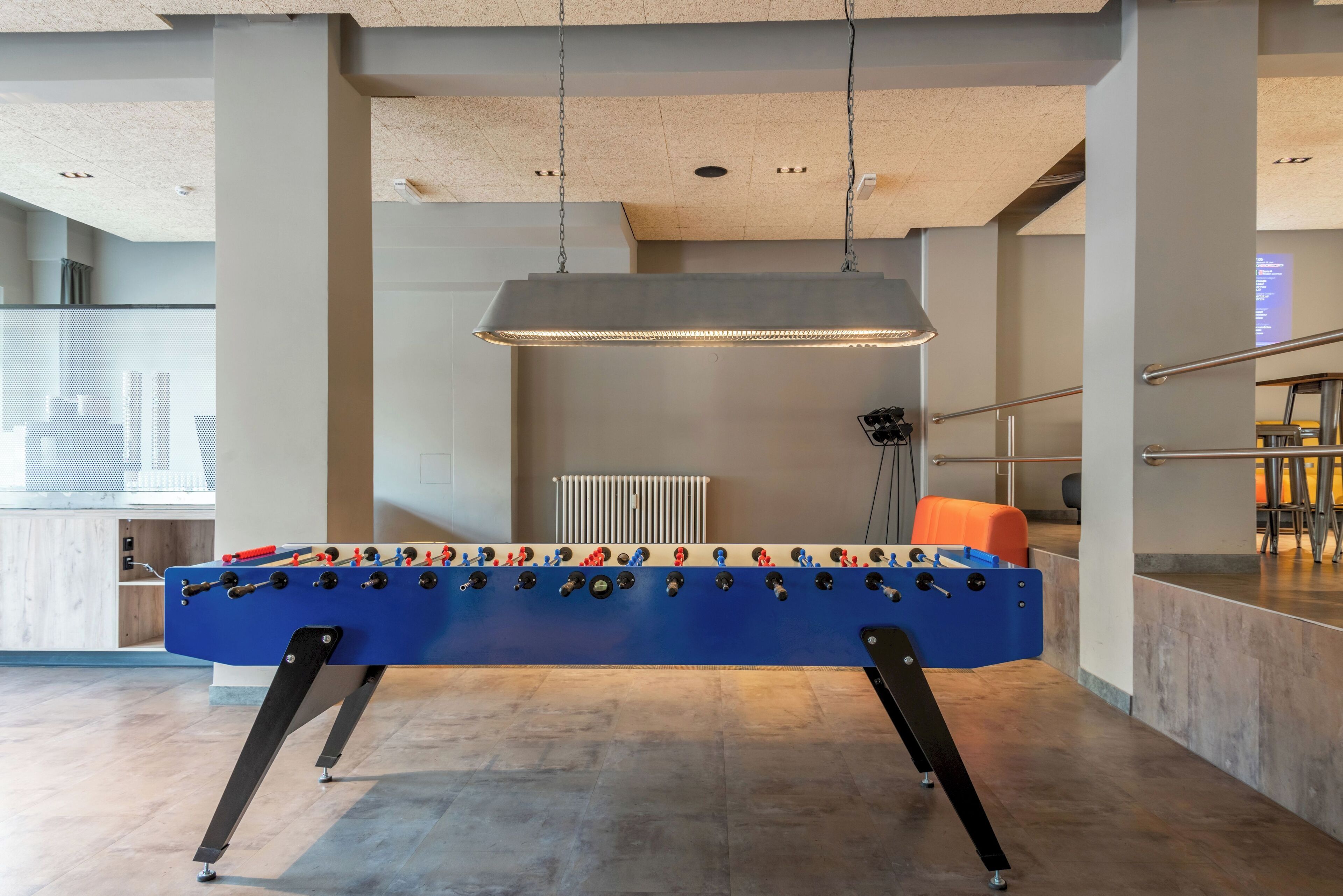 A modern indoor space with a foosball table, a hanging pendant light, and a view of a cityscape through a glass wall.