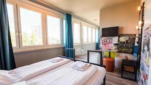 Hotellihuone, jossa on kaksi sänkyä, televisio, pieni pöytä ja näkymä kaupunkiin.