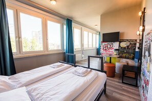 Ein Hotelzimmer mit zwei Betten, einem Fernseher, einem kleinen Tisch und Blick auf die Stadt.
