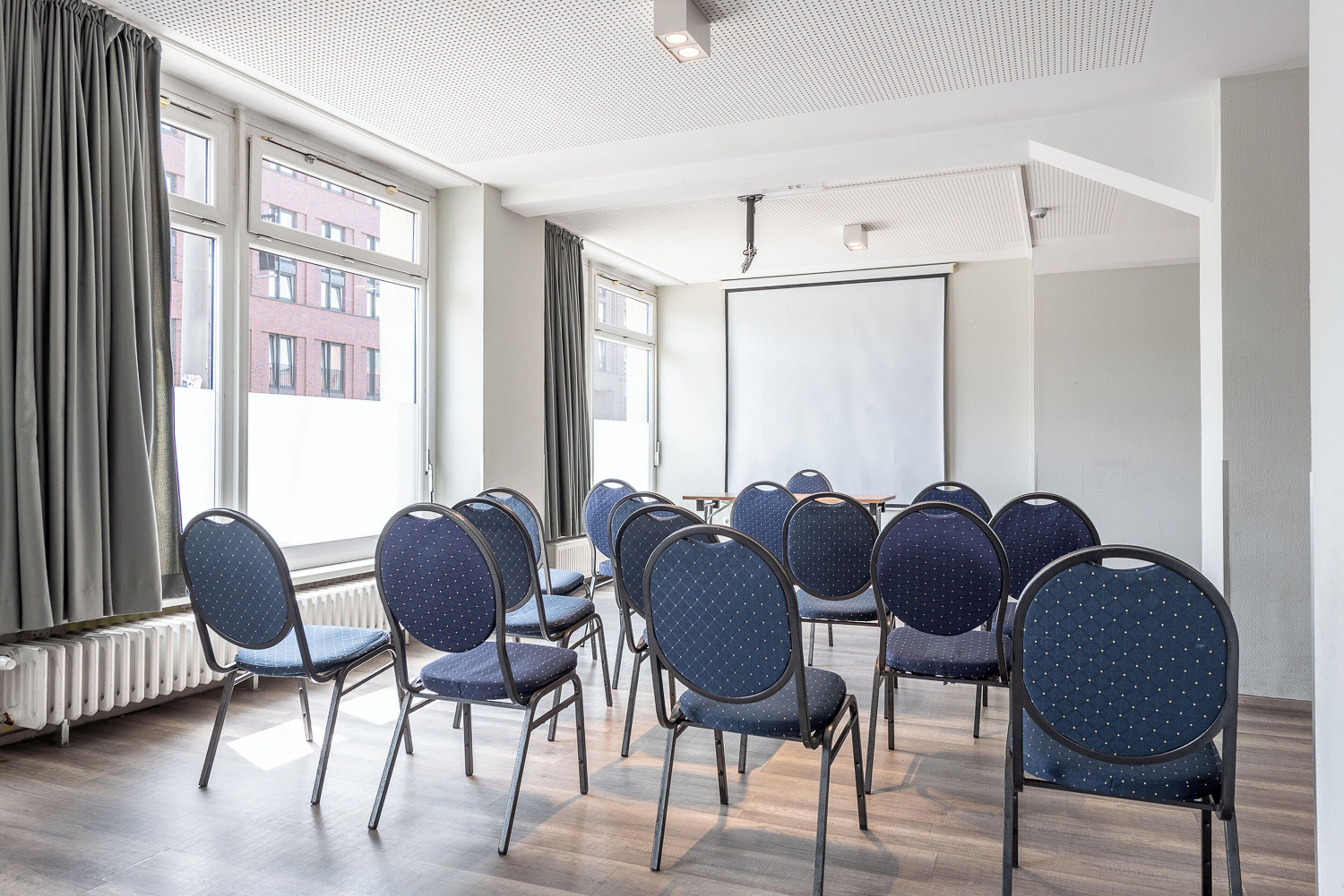 A conference room with rows of chairs, a whiteboard, and large windows with curtains.