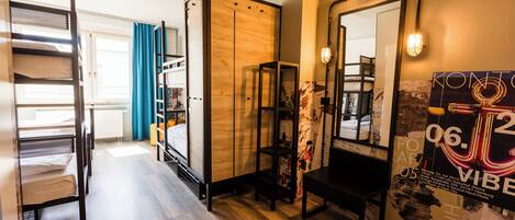 A hotel room with bunk beds, a wooden wardrobe, a mirror, and a poster on the wall.