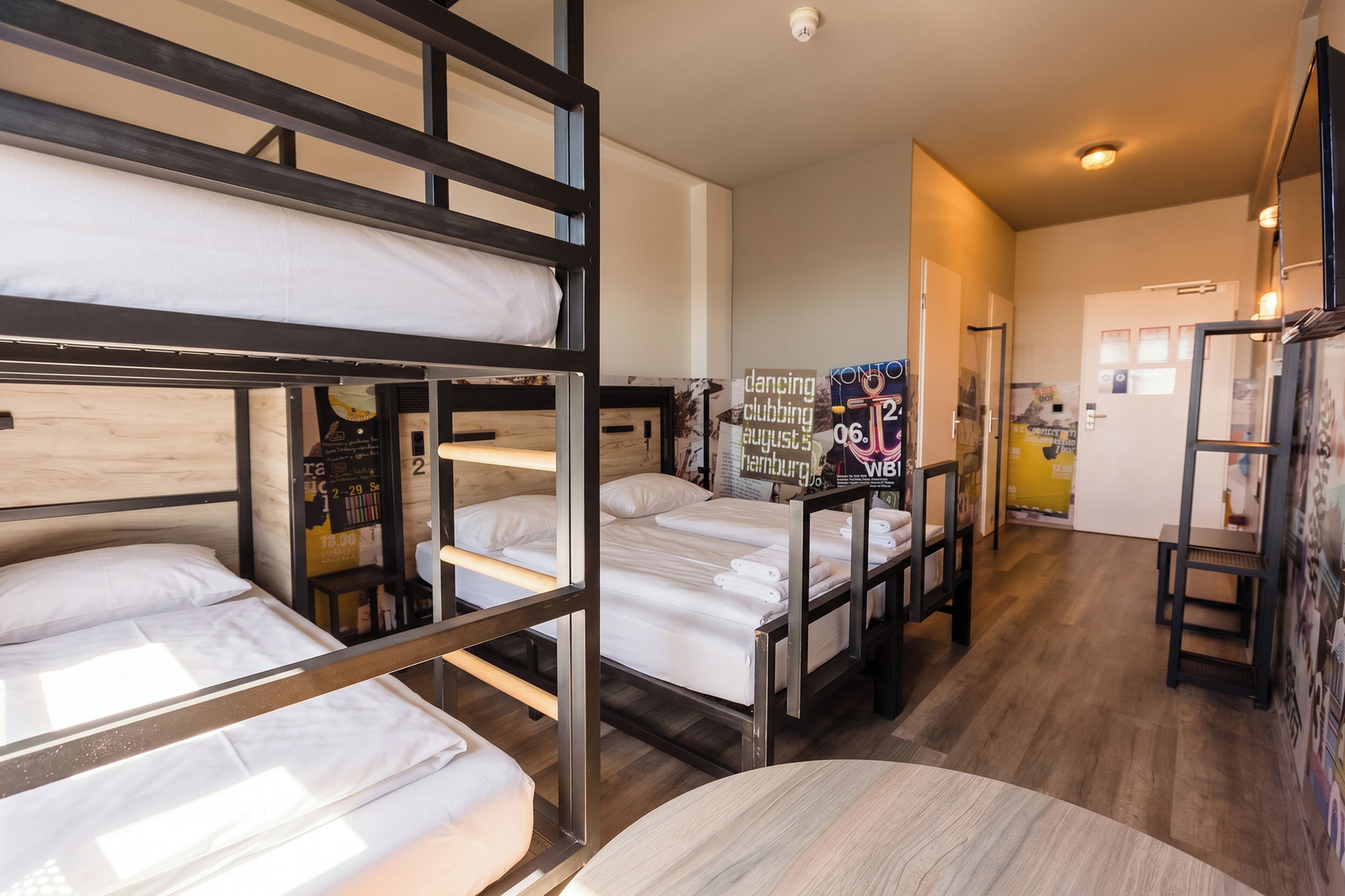 A dormitory room with bunk beds, a small table, and a poster on the wall.