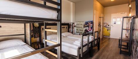 A dormitory room with bunk beds, a small table, and a poster on the wall.