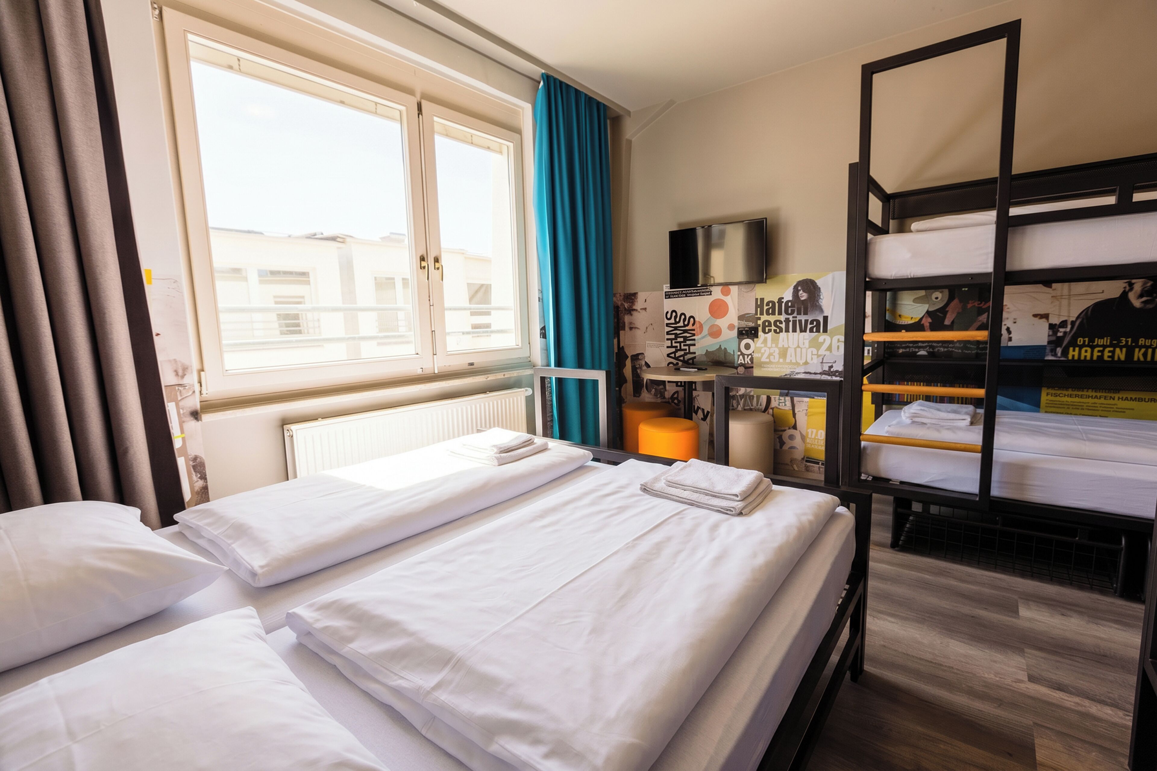 Ein Hotelzimmer mit zwei Betten, einem Fenster mit Vorhängen, einem Etagenbett, einem Fernseher und einem Poster an der Wand.