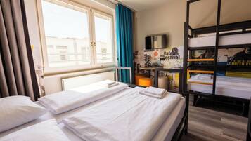 Habitación de hotel con dos camas, una ventana con cortinas, una cama litera, un televisor y un cartel en la pared.