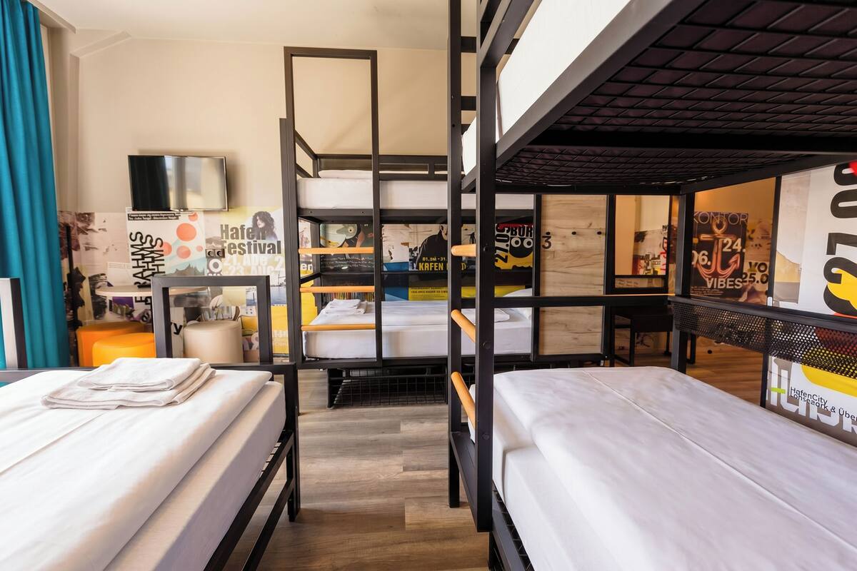 Hotellihuone, jossa on kerrossängyt, televisio, työpöytä ja julisteita seinillä.