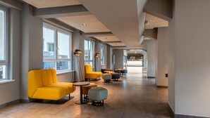 Moderni hotellin aula, jossa on suuret ikkunat, keltaiset istuimet ja pitkä käytävä, joka johtaa vastaanottoalueelle.