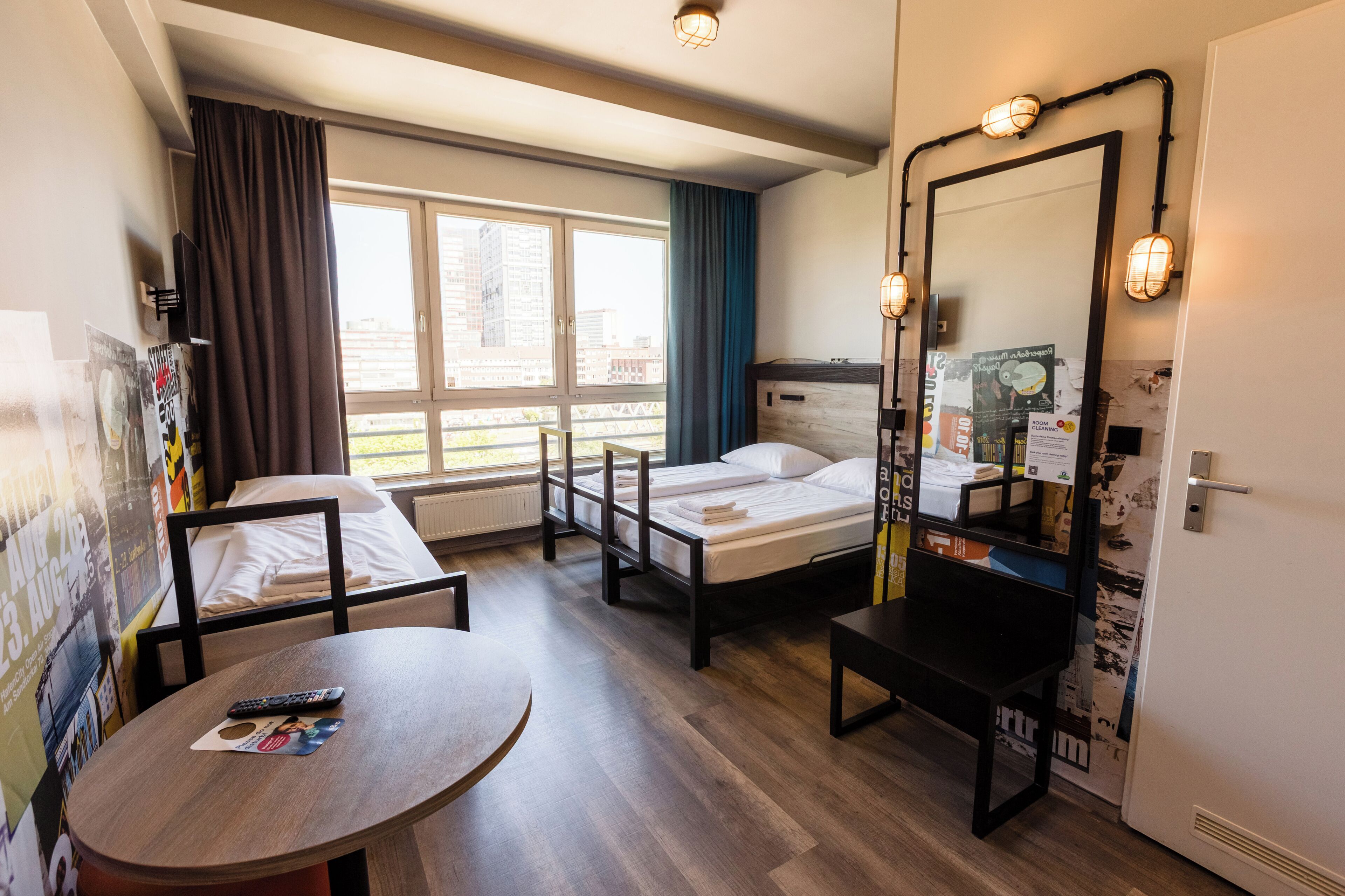 A hotel room with a bed, a desk, a chair, a round table, a mirror, and a window with curtains.