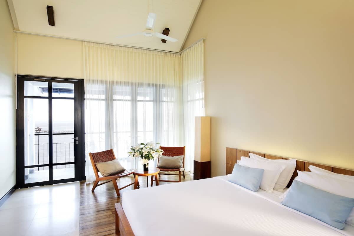 Ein Hotelzimmer mit einem großen Bett, zwei Sesseln, einem kleinen Tisch mit einer Pflanze und einer Balkontür.