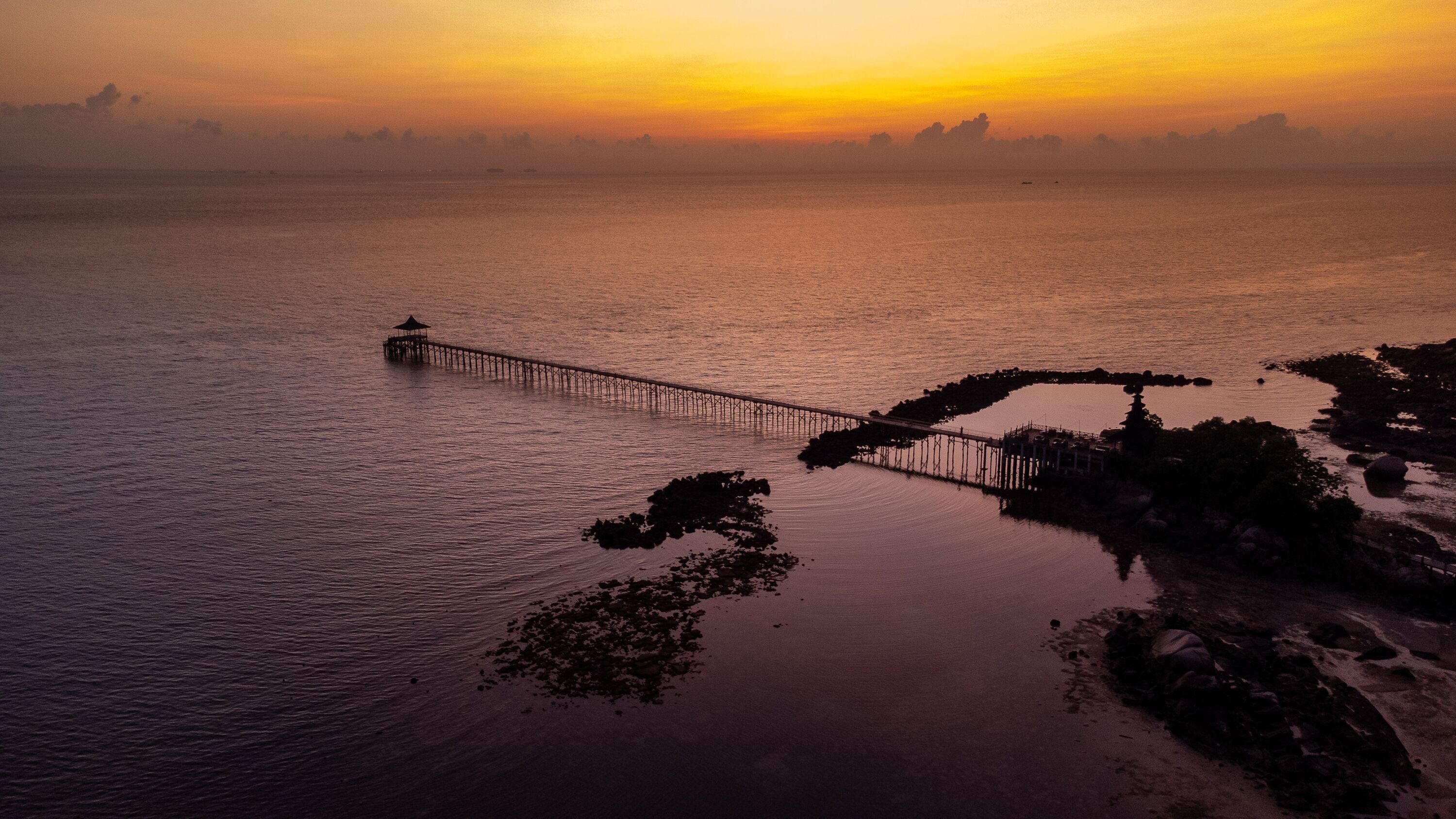 Um cais se estendendo sobre águas calmas ao pôr do sol.