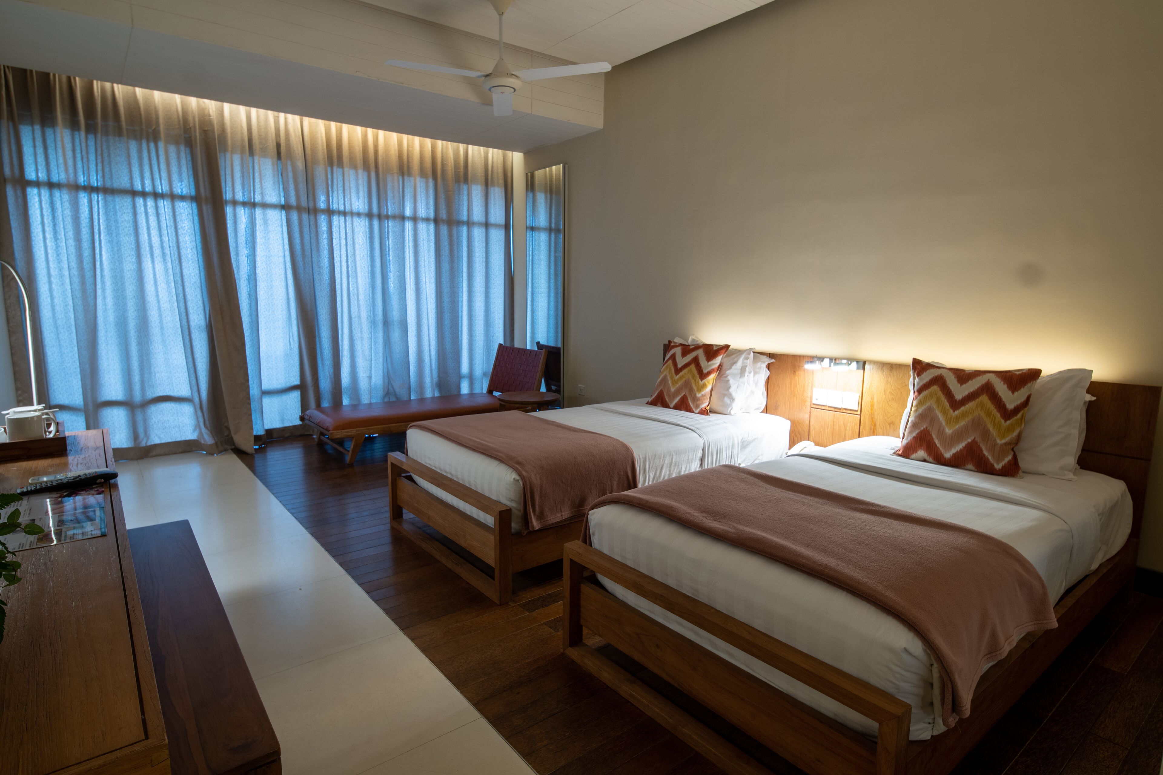 A hotel room with two beds, a desk, a chair, and a large window with curtains.