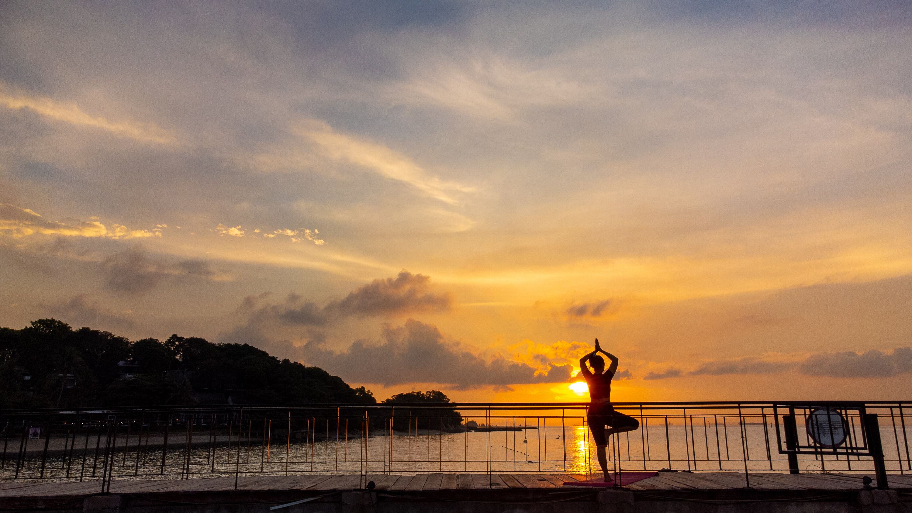 A sunset over a body of water with a person practicing yoga on a dock.