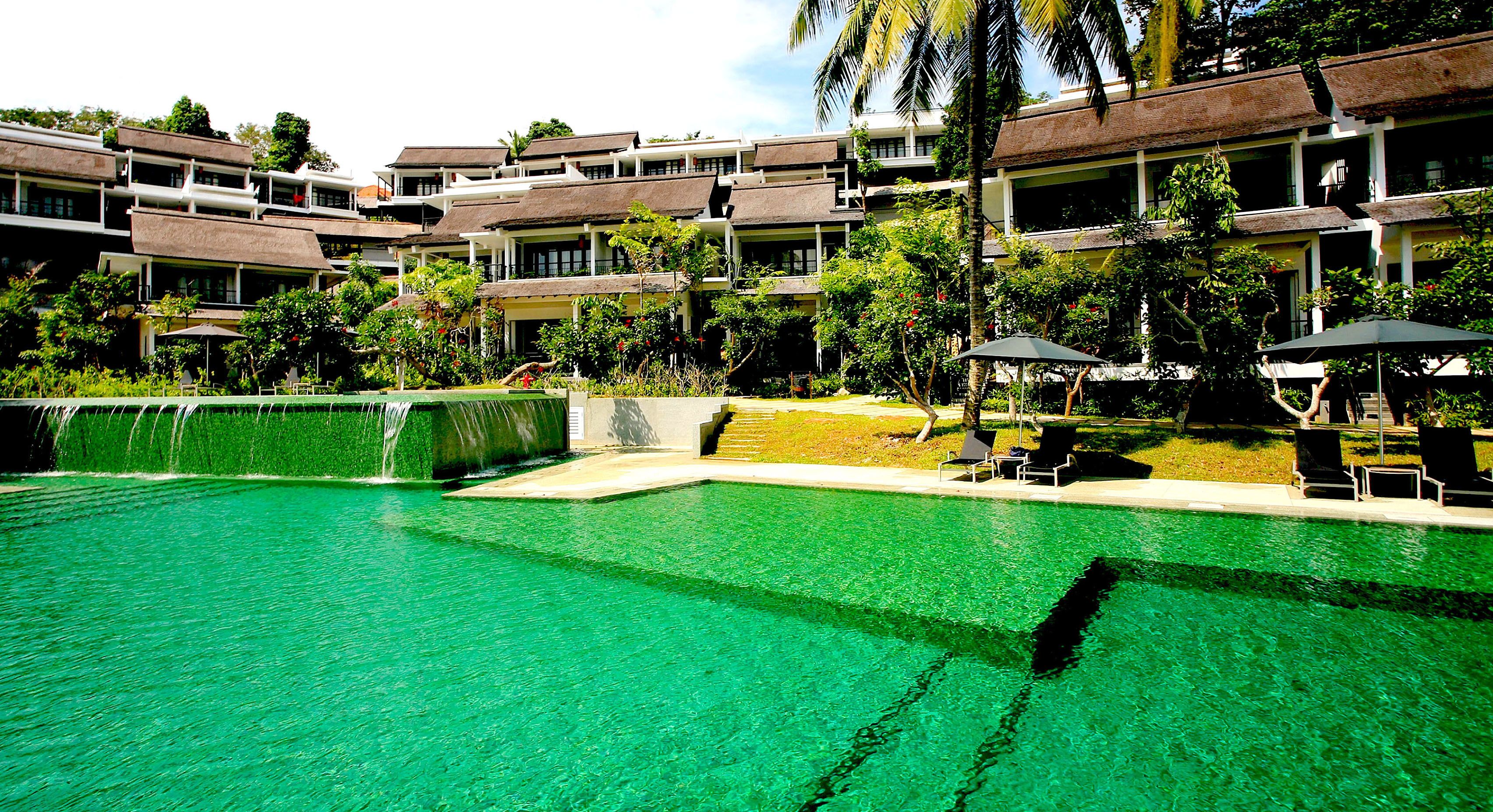 Un hotel con piscina, mobiliario exterior y abundante vegetación.