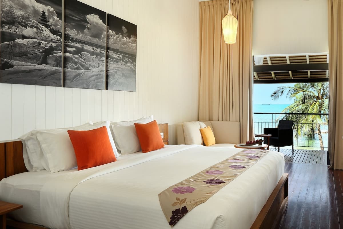 Ein Hotelzimmer mit einem großen Bett, einem Schlafsofa, einem Balkon mit Meerblick und einem Bild an der Wand.