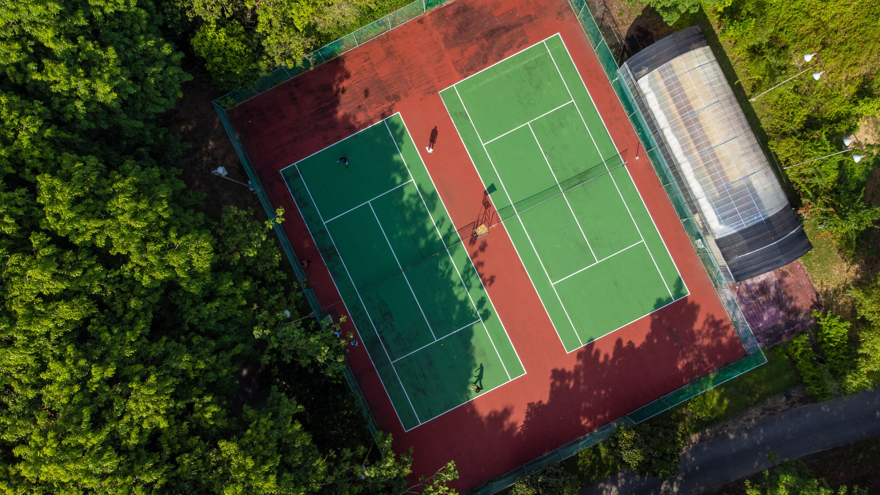 Vista aérea de una cancha de tenis rodeada de abundante follaje verde.