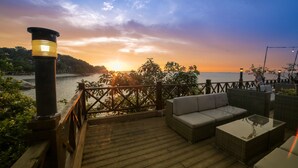 Una terraza de madera con mobiliario exterior y vistas a la puesta de sol sobre el agua.