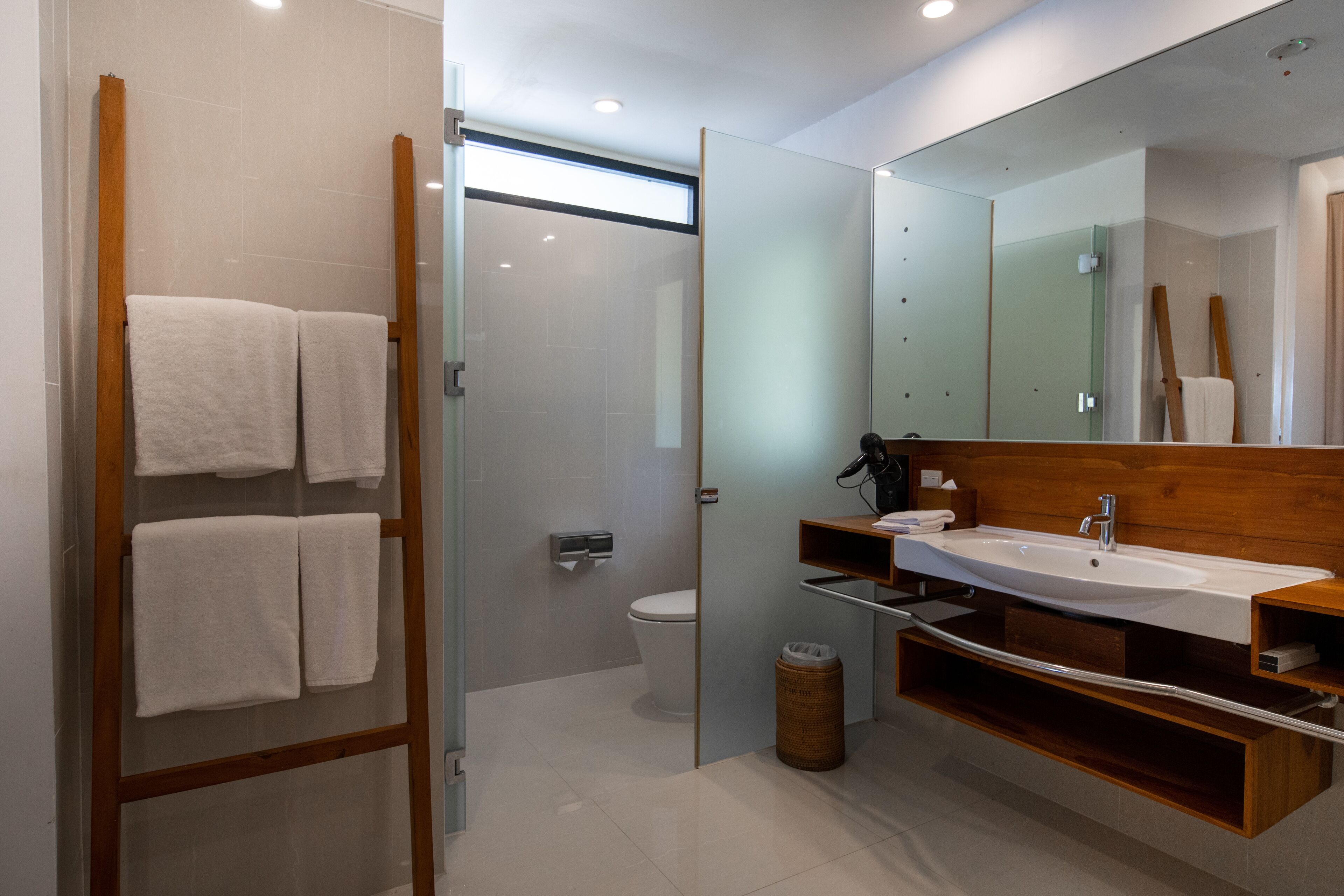 Un baño moderno con cabina de ducha de vidrio, tocador de madera con lavamanos y un espejo grande.