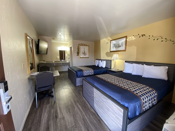 Habitación de hotel con dos camas, un escritorio, una silla, un espejo y una televisión.