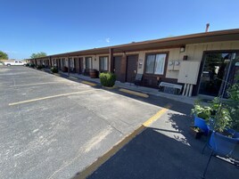 Un motel con una hilera de habitaciones, un estacionamiento y un pequeño jardín.