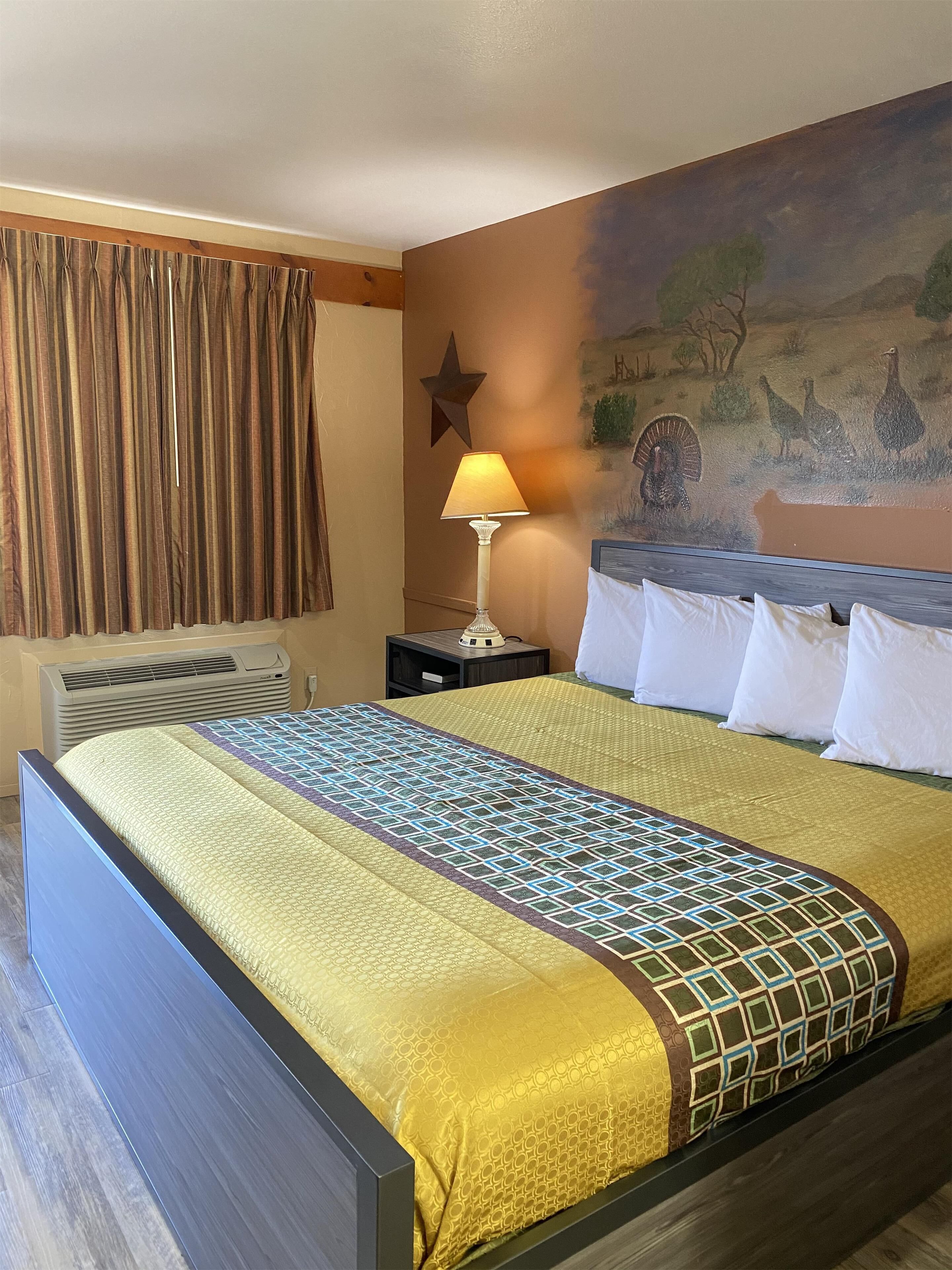 Ein Hotelzimmer mit Bett, Nachttisch, Lampe, Wandgemälde und Klimaanlage.