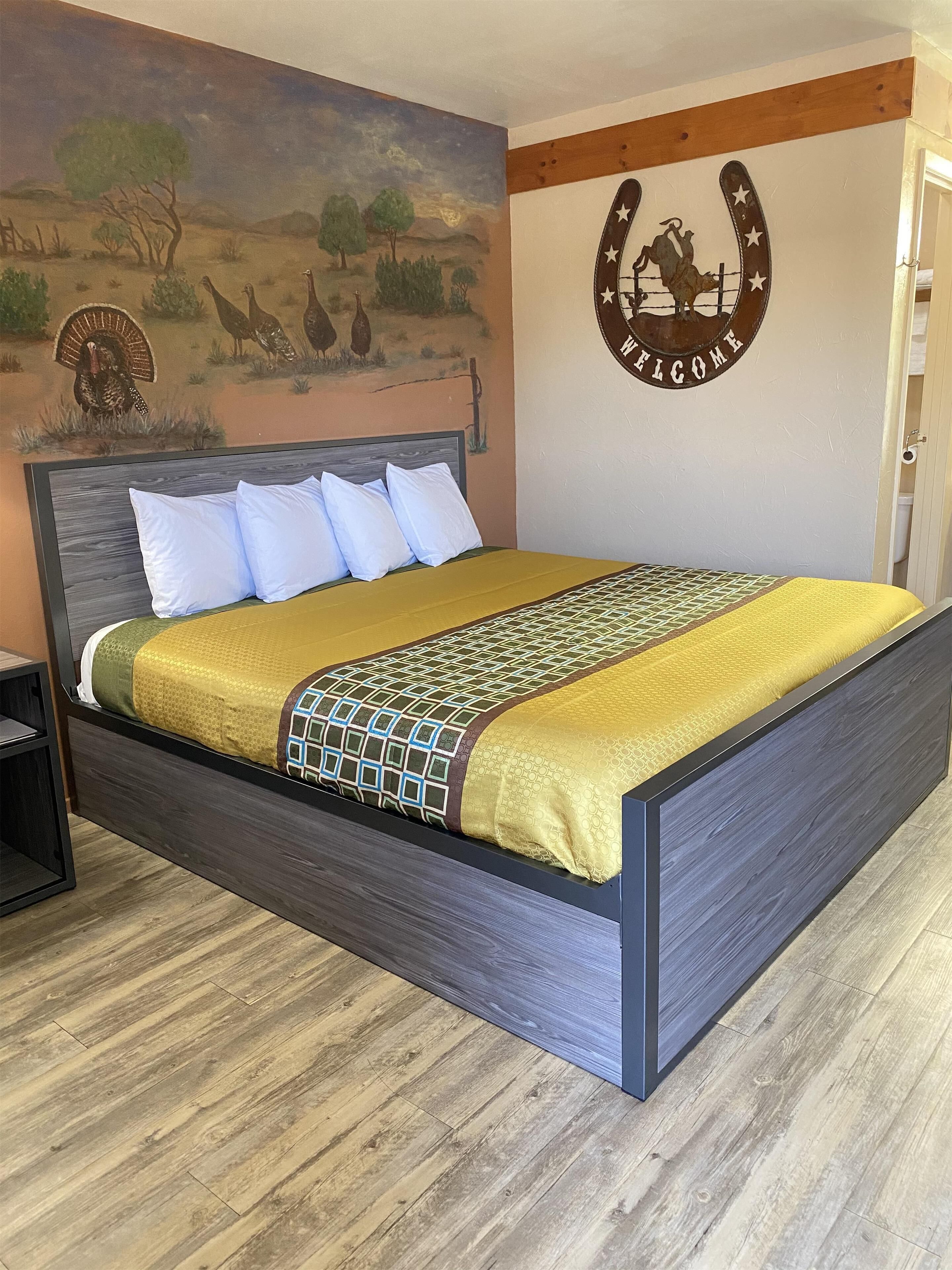 Una cama con cabecera, un mural en la pared y un cartel de bienvenida.