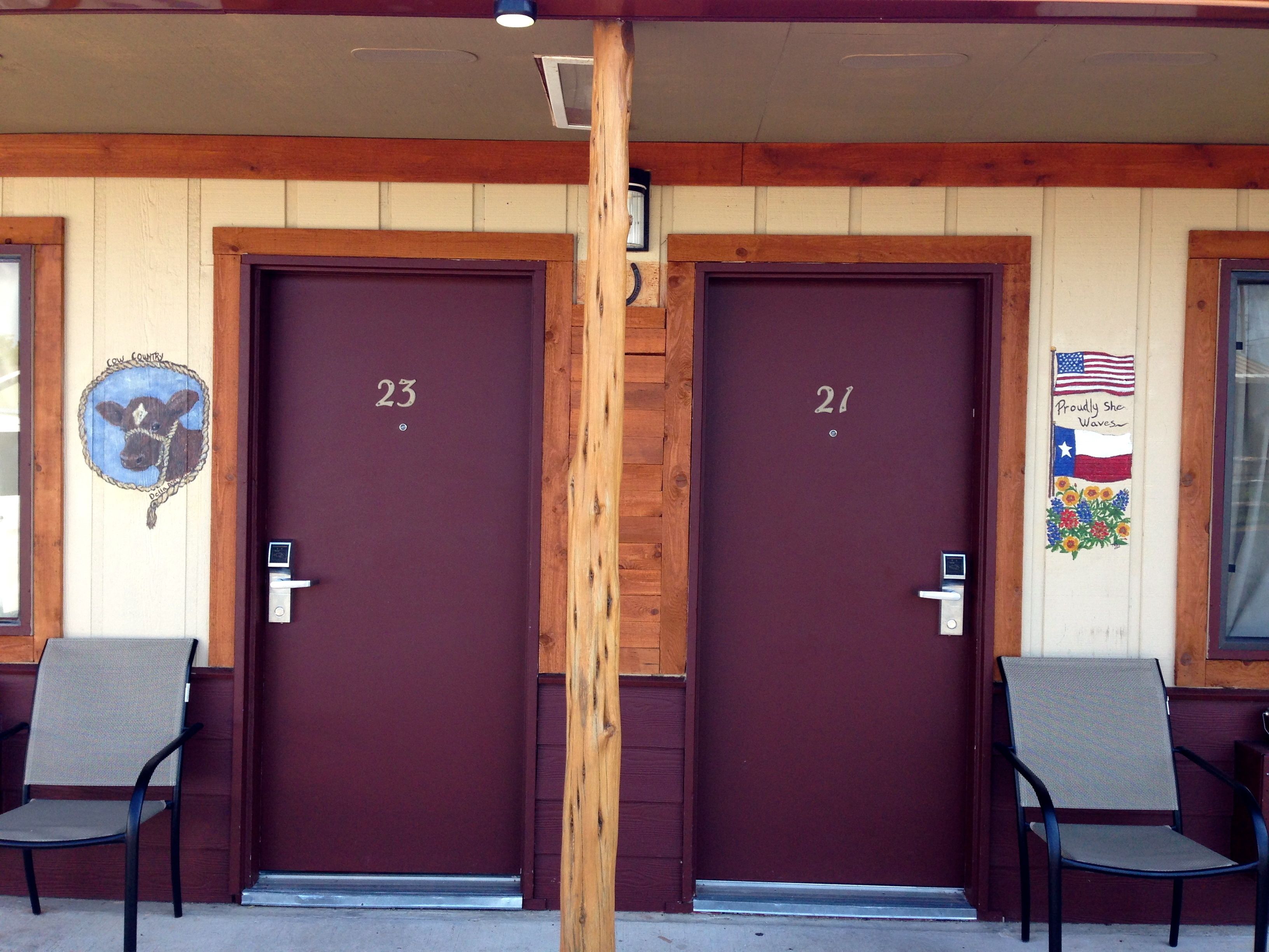 Two doors with numbers 23 and 21, a cow decoration, and a Texas flag with flowers.