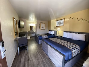 A hotel room with a bed, desk, chair, and a small kitchenette.