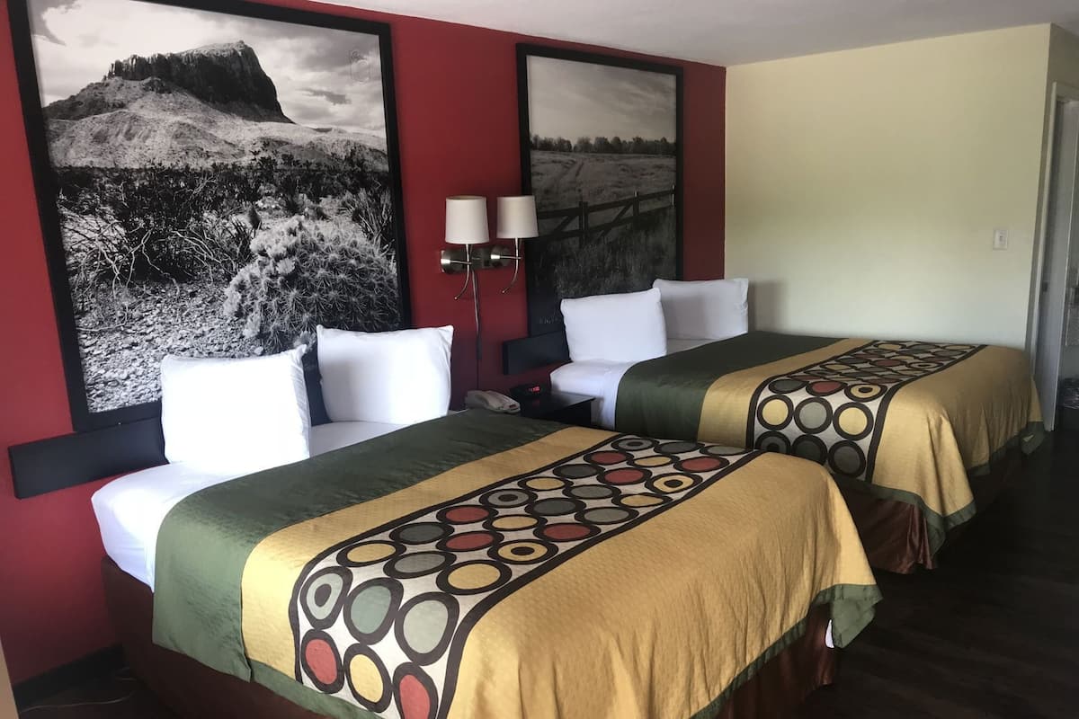 A hotel room with two beds, a red wall, and two large black-and-white landscape paintings.