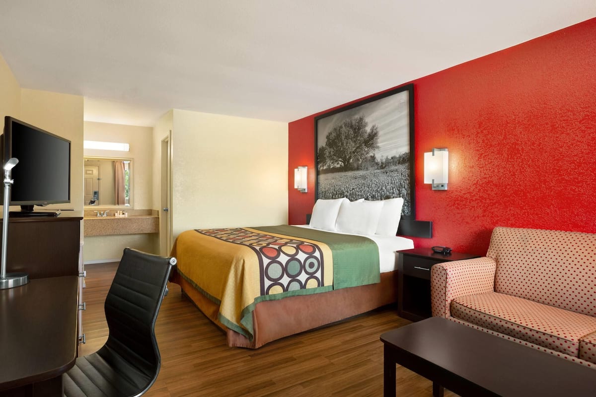 A hotel room with a bed, a desk, a chair, a sofa, and a TV.