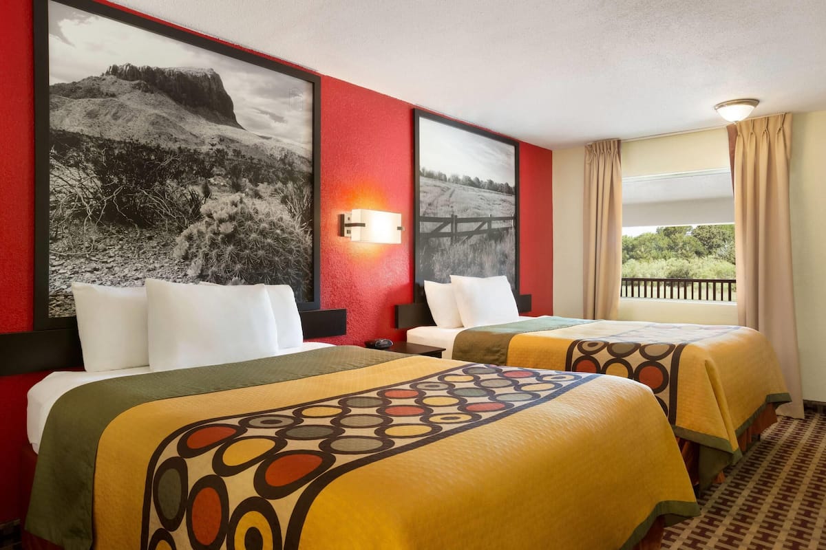 A hotel room with two beds, a red accent wall, and a large window with a view.