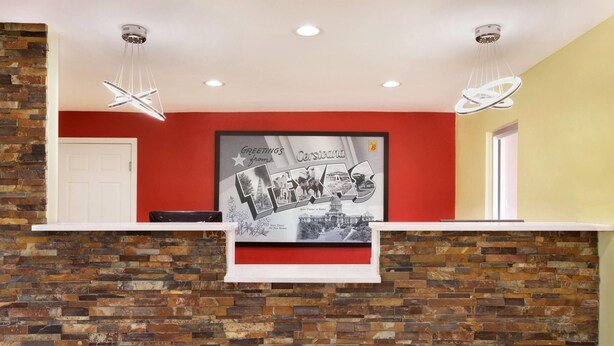 A reception desk with a red wall, a framed welcome sign, and a brick-patterned wall.