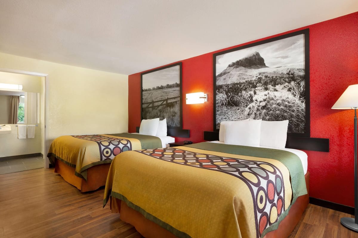 A hotel room with two beds, a red accent wall, and a framed black and white landscape painting.