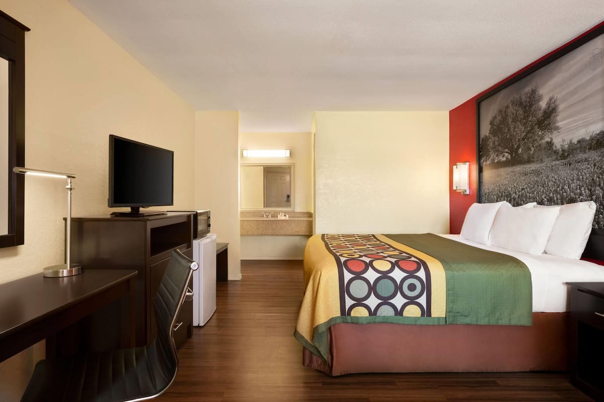 A hotel room with a bed, a desk with a television, a mirror, and a bathroom visible through an open door.