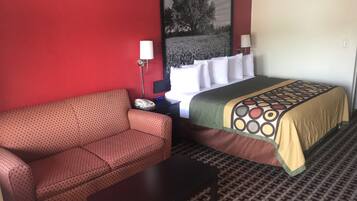 A hotel room with a red wall, a bed with a patterned bedspread, a red polka dot sofa, a small table, and a nightstand with a lamp.