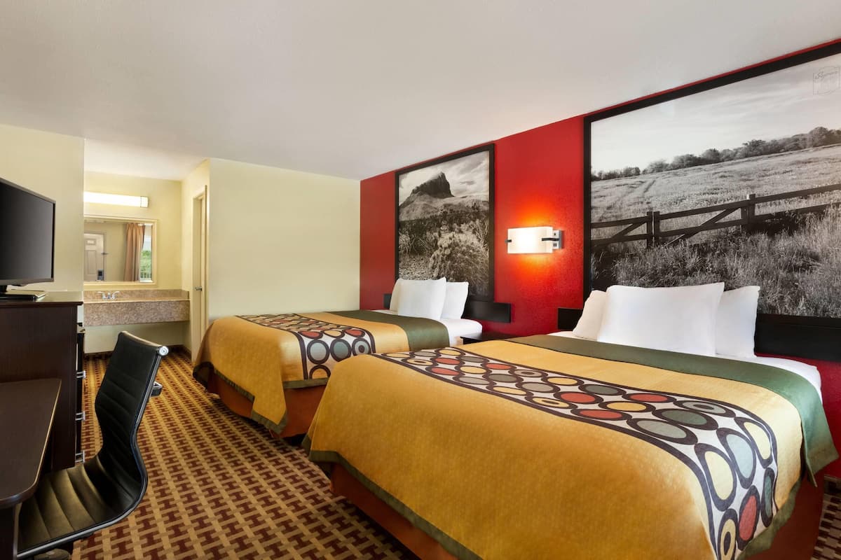 A hotel room with two beds, a desk, and a TV.