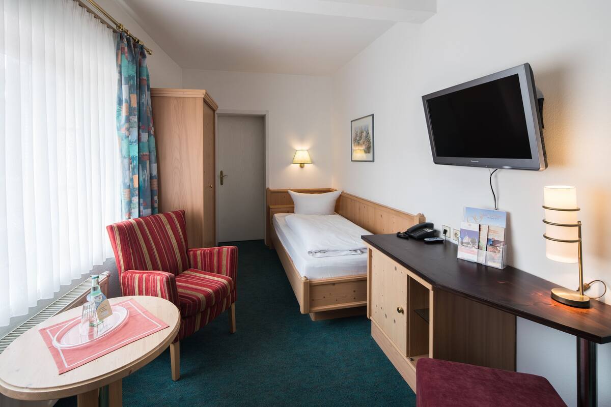 A hotel room with a bed, a desk, a chair, a TV, a lamp, and a window with curtains.