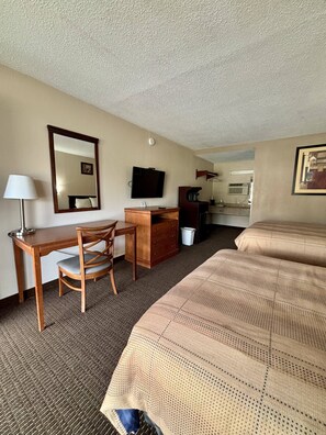 A hotel room with a bed, a desk with a chair, a television, a dresser, and a bathroom visible through an open door.