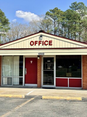 A building with a sign reading 'OFFICE' above the entrance, a number '18940' on the door, and a sign instructing to 'CHECK IN WINDOW ON YOUR RIGHT'.