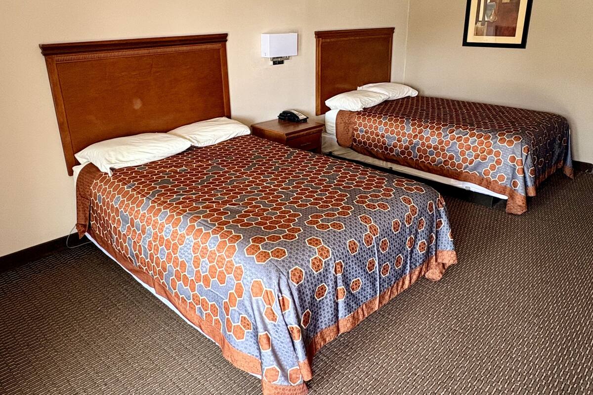 A hotel room with two beds, a nightstand, a wall-mounted lamp, and a framed picture on the wall.